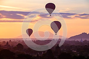 Hot air balloons fly over the ancient pagodas of old Bagan in Myanmar at sunrise.