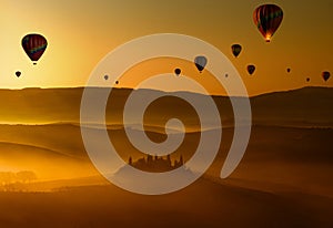 Hot air balloons flying at dawn above the misty hills in Tuscany