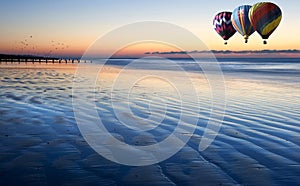 Hot air balloons over low tide beach at sunrise