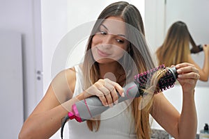 Hot air hair brush. Portrait of young woman using round brush hair dryer to style hair in an easy way at home. Girl using electric