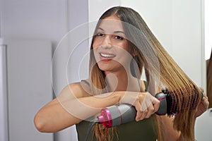 Hot air hair brush. Young woman using round brush hair dryer to style hair in an easy way at home. Teenager using electric blowout