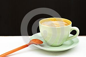 Hot Americano coffee with creamy foam on top. Put it in a green glass and saucer. With an orange spoon on the side of a white