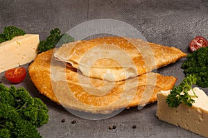 Hot appetizer: cheburek with cheese on a gray background