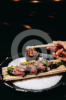 Hot appetizer Veal Tataki on a wooden tray and a piece of dish in Chinese chopsticks