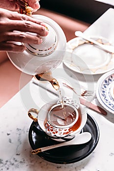 Hot Apple Tea served by pouring from mug through stainless steel tea strainer infuser in porcelain vintage cup