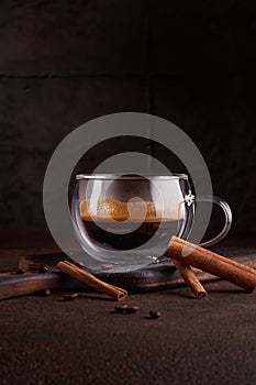 Hot and aromatic coffee spilling from glass cup on the dark background