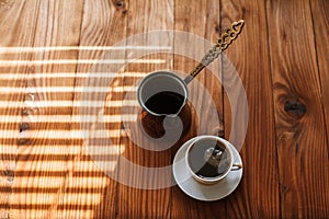 Hot aromatic coffee in a white porcelain cup on a saucer on a wooden table in the morning.