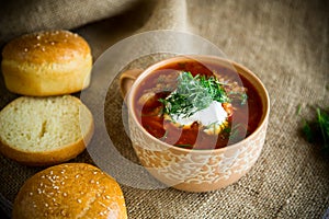 Hot beetroot soup with sour cream, herbs and rolls in a ceramic bowl