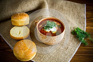 Hot beetroot soup with sour cream, herbs and rolls in a ceramic bowl