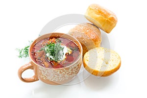 hot beetroot soup with sour cream, herbs and rolls in a ceramic bowl