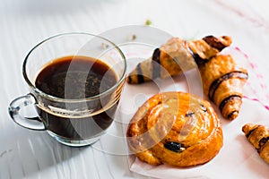 Hot black coffee in clear cup, with bakery placed on white wood table, With sunshine in morning,Beauty concept of beverage and