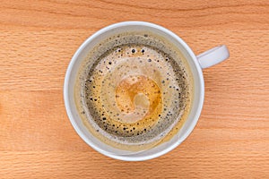 Hot black coffee with foam bubbles in white cup with wooden boar