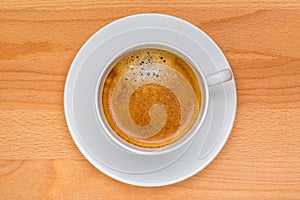 Hot black coffee with foam bubbles in white cup with wooden boar