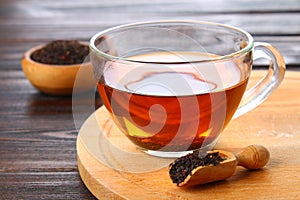 Hot black tea in a glass cup and dry tea on a wooden table.