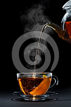 hot black tea pouring from teapot into glass cup with lemon