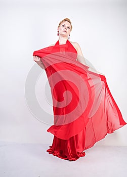 Hot blonde caucasian woman wearing long red evening dress and posing on white studio background alone. fashionable adult girl with