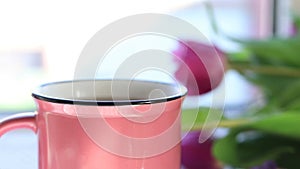 Hot boiling tea in pink ceramic cup with pairs on windowsill