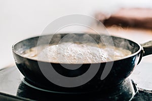 Hot boiling water in a black pan with floating steam. Boiling water for cooking spaghetti