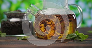 hot boiling water pours into glass teapot with black dried tea leaves on wooden table