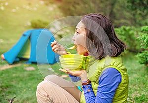 Hot breakfast in the woods - Woman hiker eating hot meal near the tent while camping in mountains