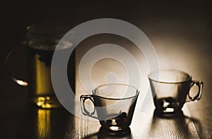 Hot brewed tea in transparent teapot and two cups on wooden background
