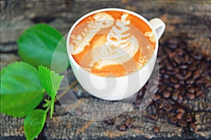 Hot cappuccino with coffee bean and green leaf on wood table