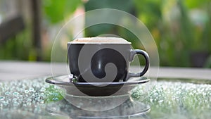 Hot cappuccino coffee cup on grass table in garden with dewdrop