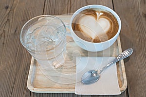 Hot cappuccino coffee with ice water on wood table