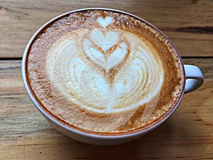 Hot cappuccino coffee in white cup and saucer with spoon on wooden table background.