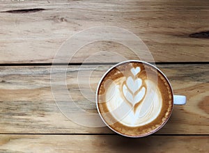 Hot cappuccino coffee in white cup on wooden table background. Art of milk foam drawing.