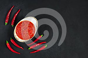 Hot chili peppers adjika sauce. Harissa sauce in a bowl on a black background. Tunisia, Georgian and Arabic cuisine. Copy space,