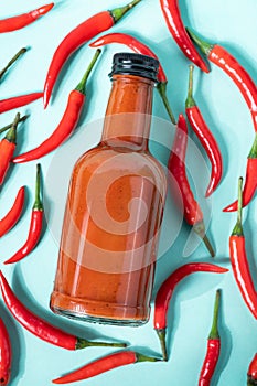 Hot chili sauce in a bottle on a bright blue background with fresh red pepper. The concept of vegetarian delicious food