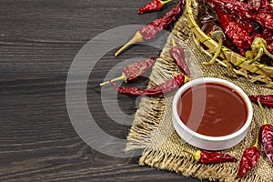Hot chili sauce in bowl with different varieties of dry hot peppers, main ingredient for preparation. Black wooden cooking