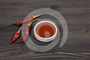 Hot chili sauce in bowl with dry hot peppers, main ingredient for preparation. Black wooden cooking background