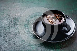 Hot chocolate with anise and nuts in black ceramic cup on old dark green concrete background. Selective focus