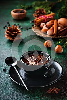 Hot chocolate with anise and nuts in black ceramic cup on old dark green concrete background. Selective focus