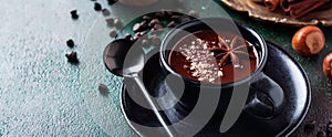 Hot chocolate with anise and nuts in black ceramic cup on old dark green concrete background. Selective focus