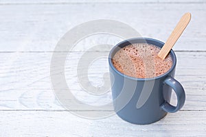 Hot chocolate in a blue-grey ceramic mug with wooden stirrer  on white painted wood. Space for text