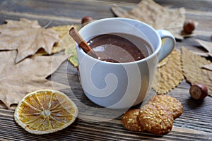 Hot chocolate with cinnamon stick in cup leaves nuts cookies dried oranges on wooden table