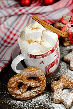 Hot chocolate or cocoa beverage with cinnamon and gingerbread cookies in snowon vintage wooden table background.