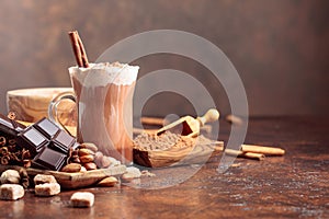Hot chocolate with cocoa powder, cream, cinnamon, chocolate pieces and other ingredients on a brown table