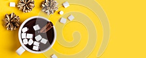 Hot chocolate cup with cinnamon and marshmallow on yellow background. Warming Christmas winter drink