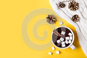 Hot chocolate cup with cinnamon and marshmallow on yellow background. Warming Christmas winter drink