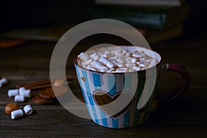 Hot chocolate drink with marshmallows in blue striped cup, stacked books on wooden rustic background. Closeup view