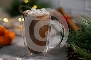 hot chocolate in a glass mug with mini marshmallows on grey table, blurred xmas background