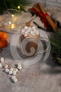 hot chocolate in a glass mug with mini marshmallows on grey table, blurred xmas background