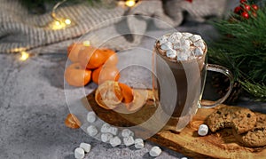 hot chocolate in a glass mug with mini marshmallows on wooden plate, blurred xmas background
