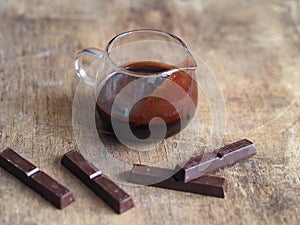 Hot chocolate icing for pouring confectionery. Pieces of chocolate on a wooden ancient background