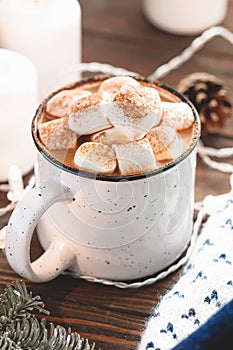 Hot chocolate with marshmallow in a white ceramic mug among winter things and decor on a wooden table