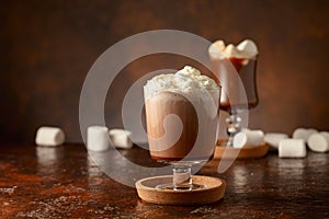 Hot chocolate with whipped cream in a glass mug on a old brown table